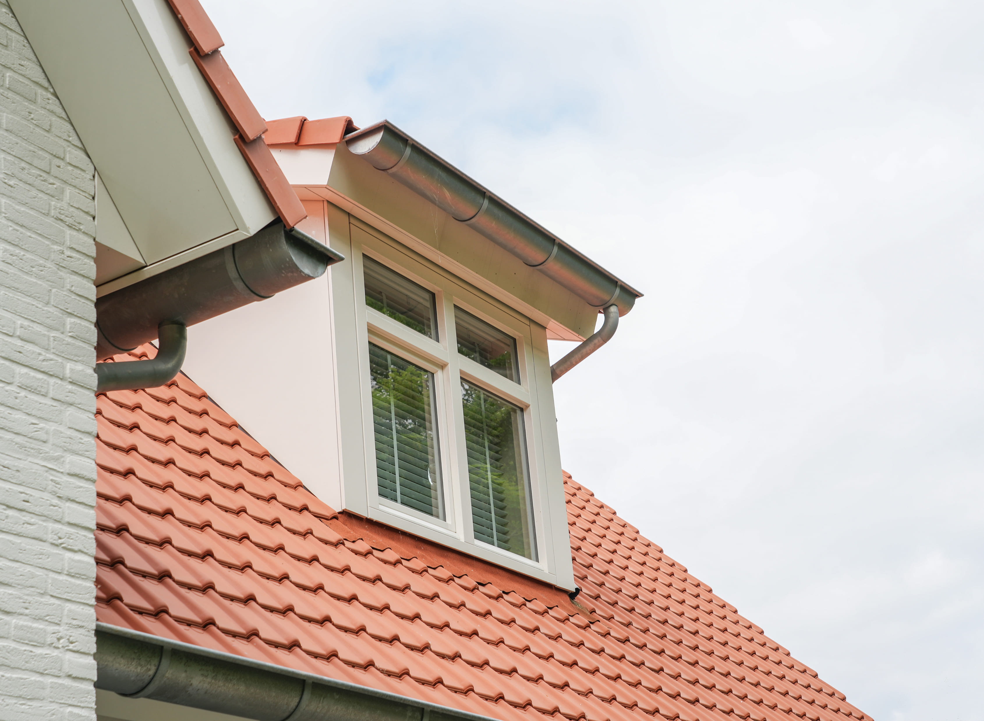 Uitsnede van dak boerderijwoning met rode dakpannen en dakkapel