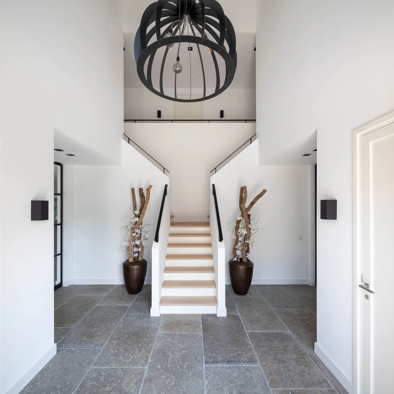 Een luxe entree met grijze tegelvloer, grote industriele lamp en vide