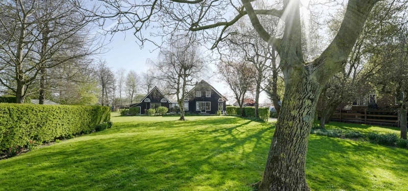 De voorzijde van een woonboerderij met een donkere gevel op een ruim perceel