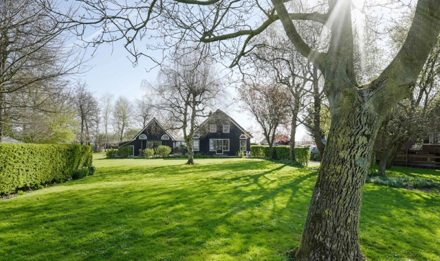De voorzijde van een woonboerderij met een donkere gevel op een ruim perceel
