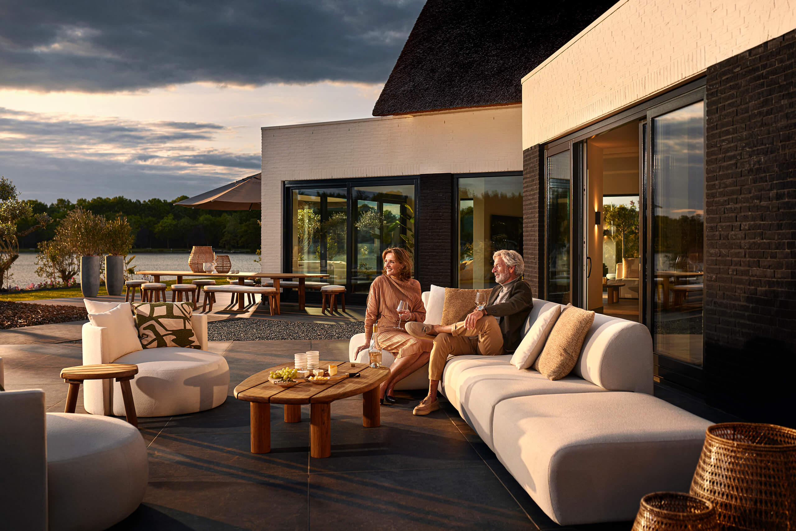 Echtpaar zit op een bank op het terras voor hun eigen maatwerk villa tijdens de avondschemering