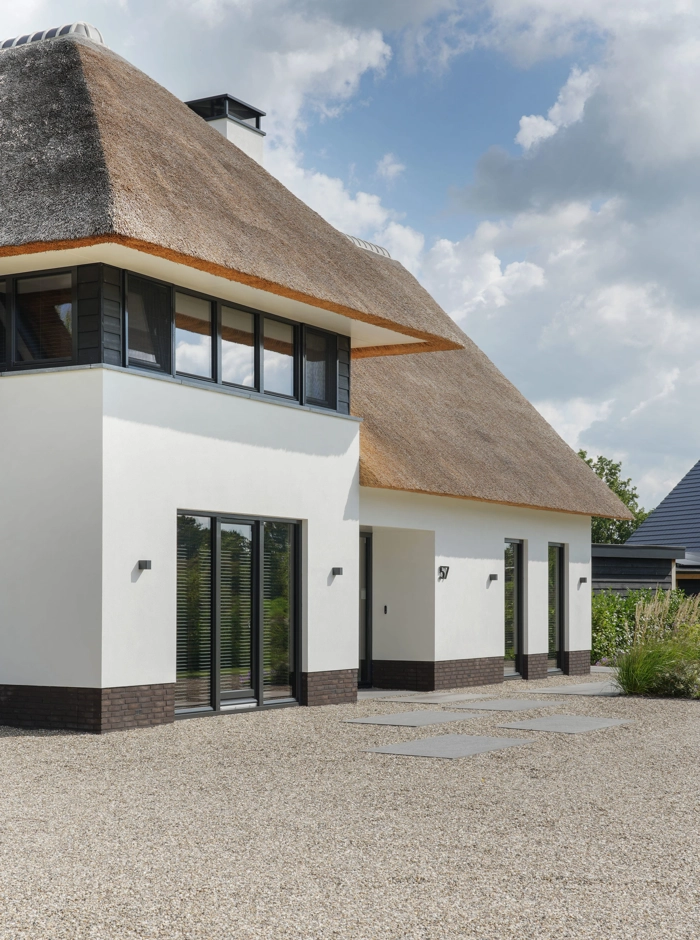 Zij-aanzicht van luxe villa met witte gevel en rieten dak