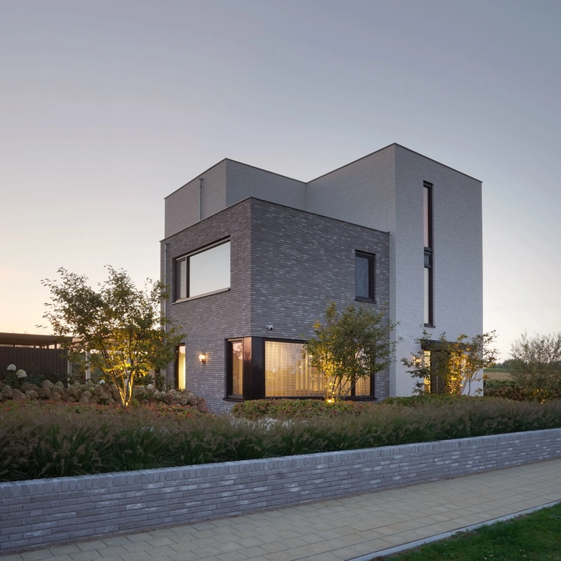 De zijgevel van een moderne, kubistische villa met wit-grijze gevelafwerking