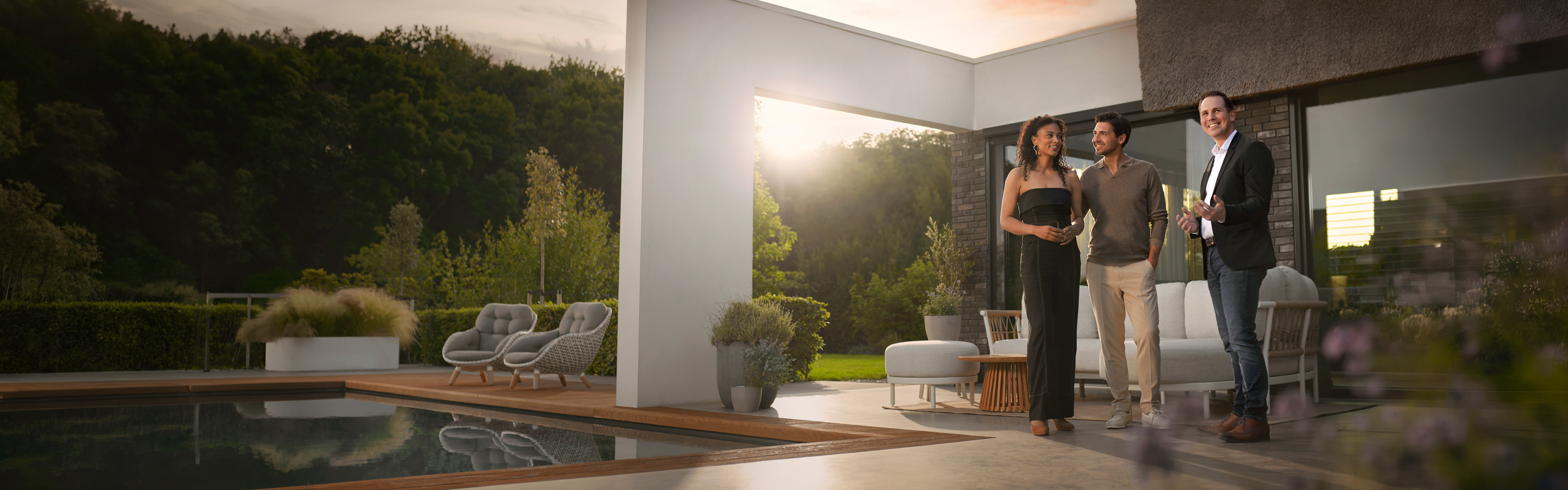 Terras met zwembad en loungeset bij zonsondergang, waar drie mensen in gesprek zijn voor een woning, door Livingstone