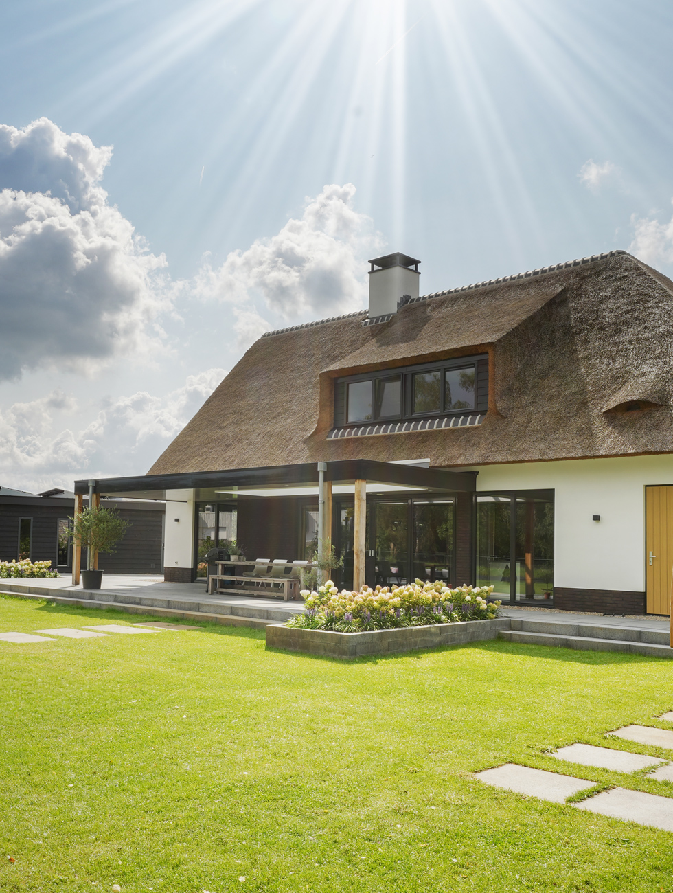 Moderne villa met rieten kap en dakkapel, overkapping met houten palen boven het terras en een zonnig gazon, door Livingstone
