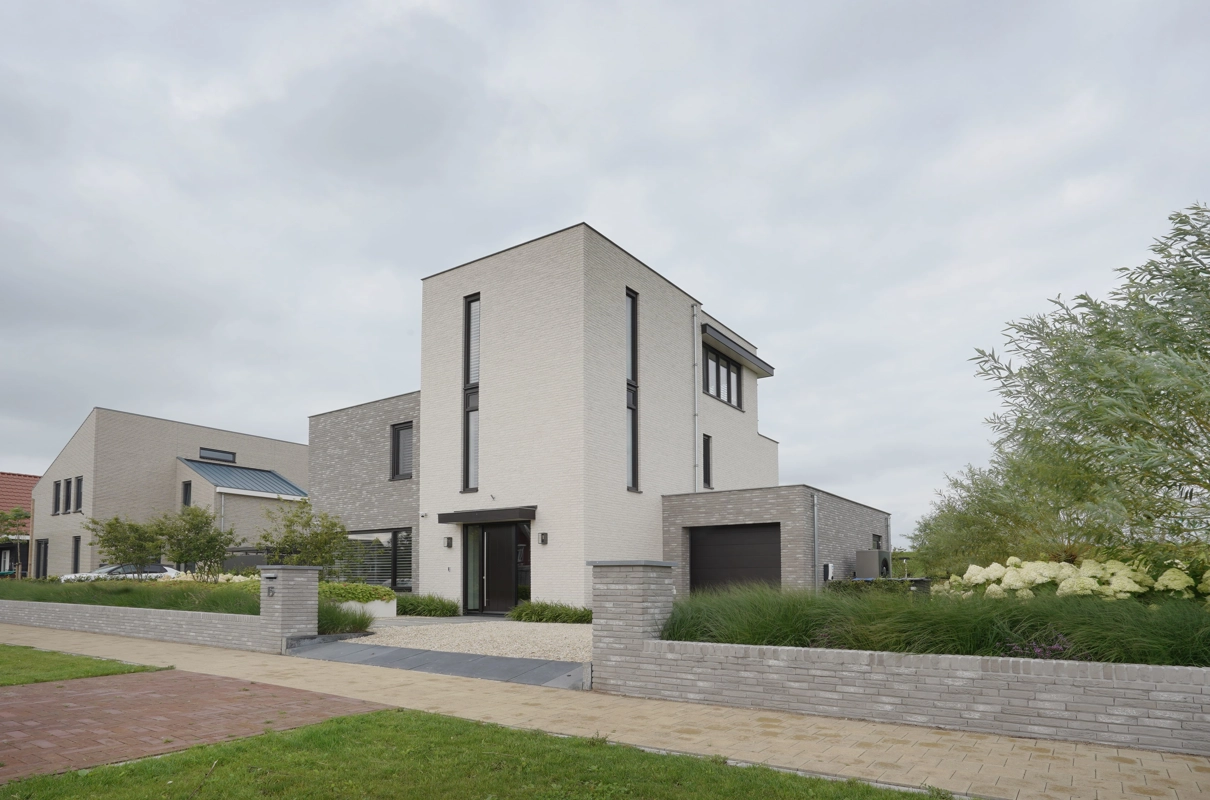 De voorgevel van een moderne, kubistische villa met wit-grijze gevelafwerking en garage