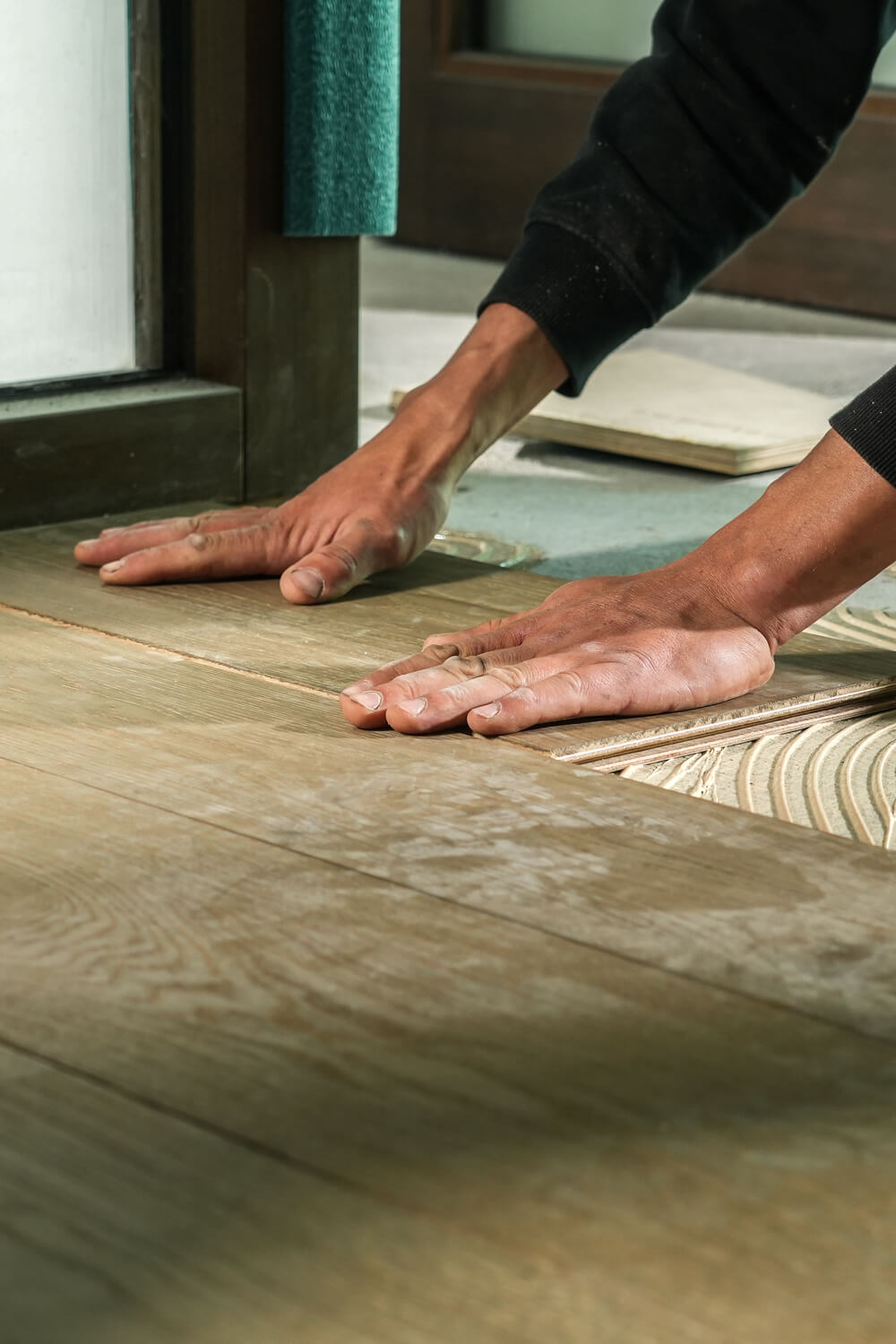 Close up van handen van een vloerenspecialst die een houten vloer legt