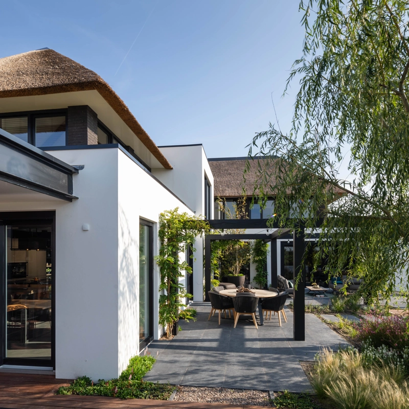 Het zijaanzicht van een kubistisch landelijke villa met wit stucwerk en rieten dak
