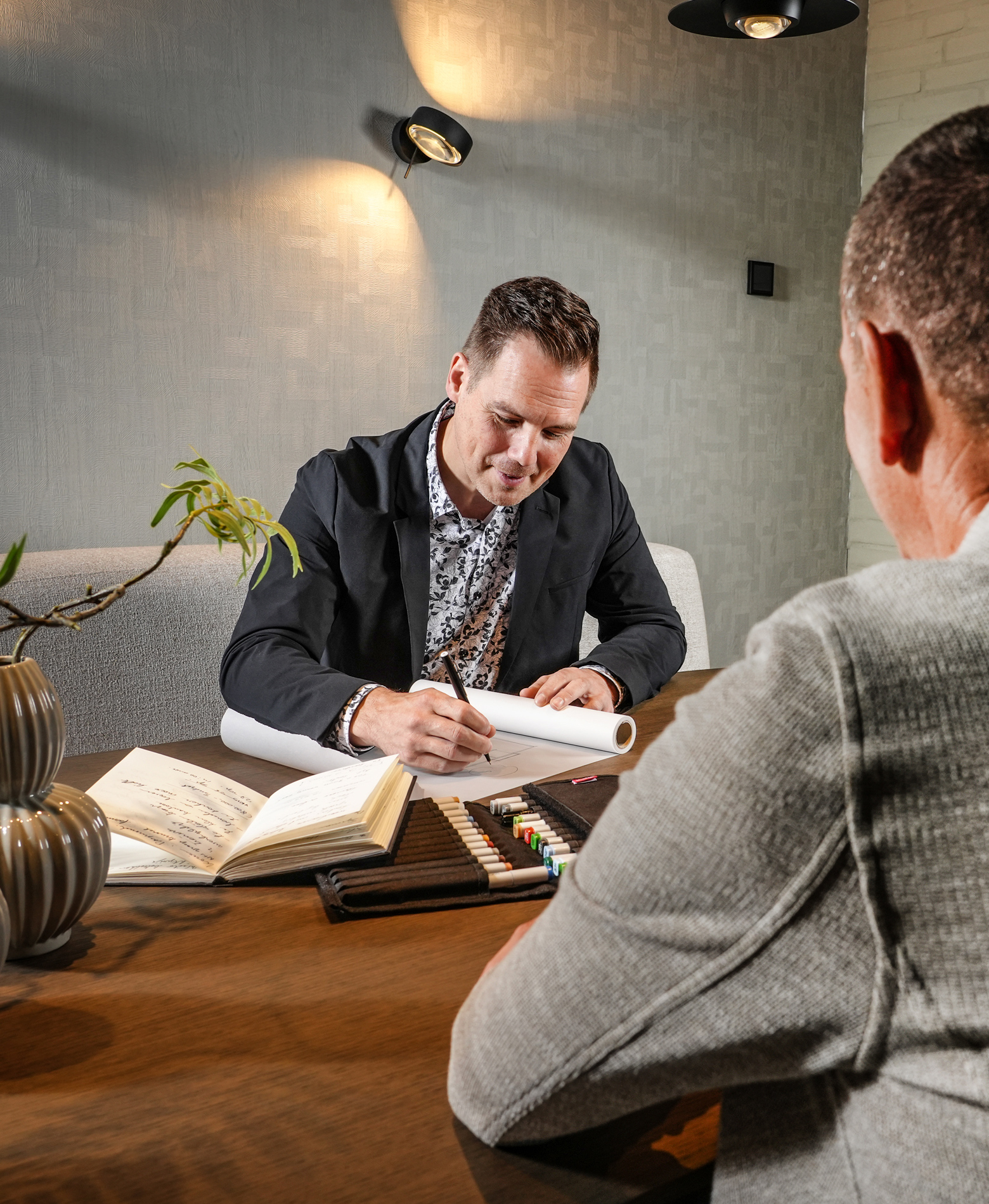 Schetsen tijdens een ontwerpgesprek bij Livingstone: een man tekent op een papierrol, met stiften en een notitieboek op tafel